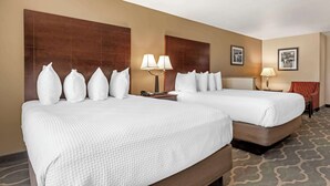 Quarto de hotel com duas camas, uma mesa de cabeceira, uma luminária e uma cadeira.