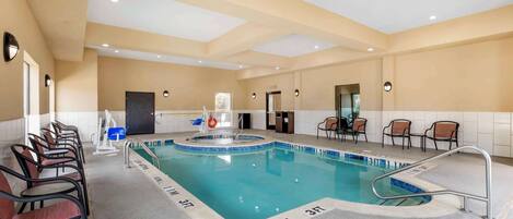 Una piscina con profundidades señalizadas, rodeada de sillas y una silla para socorrista, con un techo que incluye iluminación empotrada.