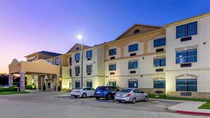 Um hotel com fachada de tijolos, várias janelas e um estacionamento com diversos carros.