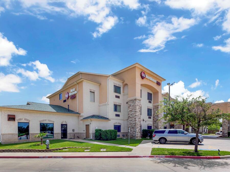 Un hotel Best Western con un edificio de dos pisos, un estacionamiento y un cielo azul despejado con nubes.