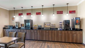 Uma cozinha de hotel com um balcão comprido, diversos eletrodomésticos e um espaço de refeições com cadeiras.