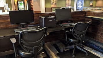 A hotel reception area with two computer workstations, a refrigerator, and a 'Corner Market' sign.