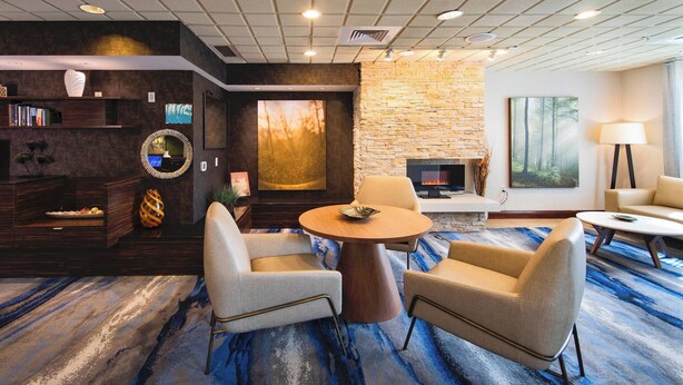 A modern lounge area with a stone fireplace, comfortable seating, and a large window with a forest view.