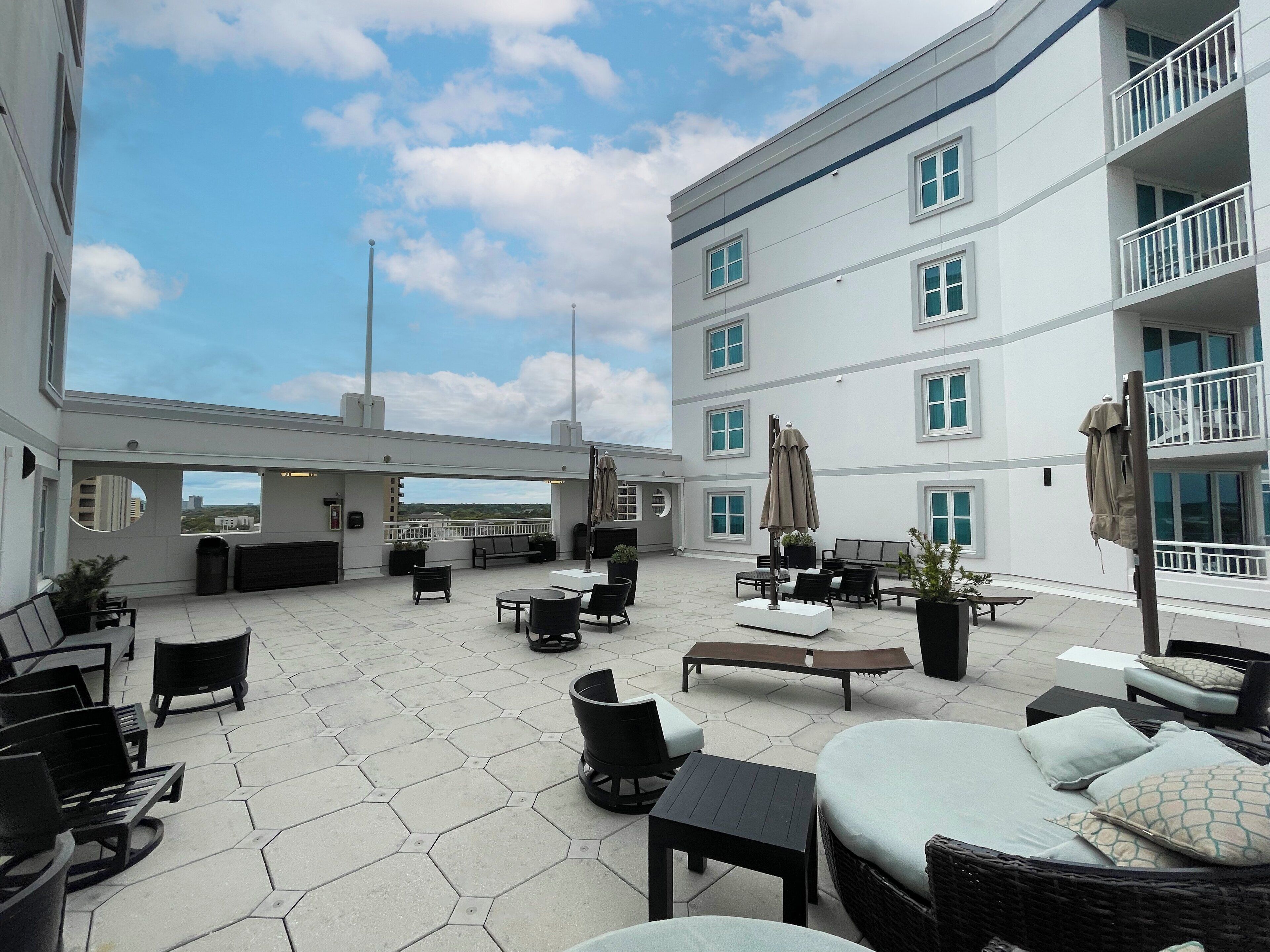 Una terraza en la azotea con mobiliario exterior, vistas a la ciudad y un edificio con balcones.