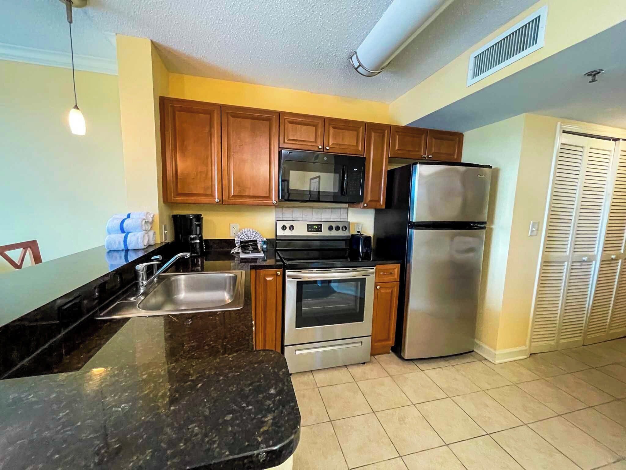 A kitchen with wooden cabinets, a stainless steel refrigerator, a microwave, an oven, and a sink.