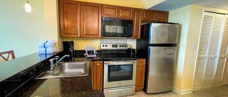 A kitchen with wooden cabinets, a stainless steel refrigerator, a microwave, an oven, and a sink.