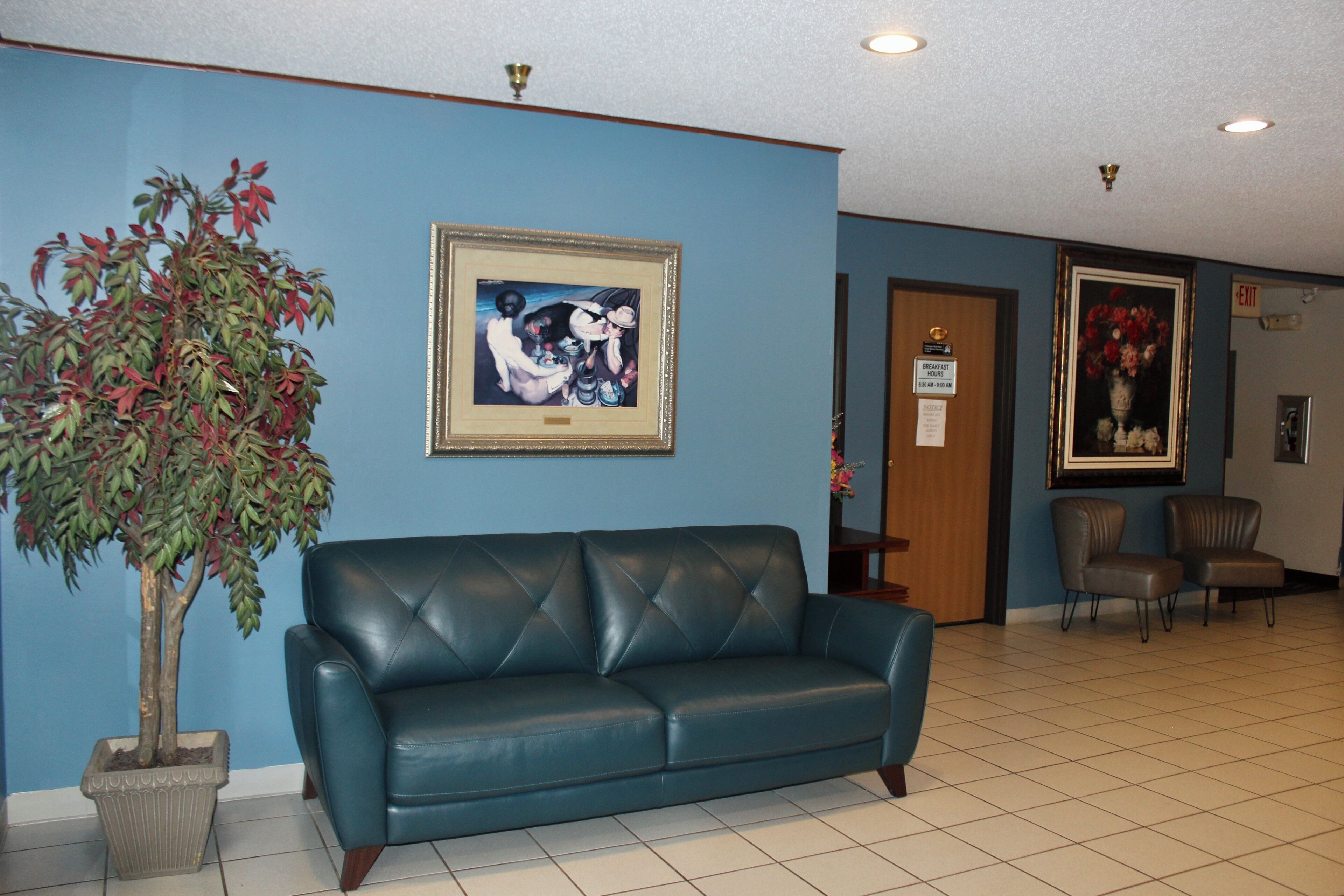 Un hall d’entrée avec un mur bleu, un tableau encadré, un canapé en cuir bleu, une plante en pot et deux chaises.