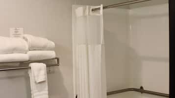 A bathroom with a shower curtain, a towel rack with folded towels, a grab bar, and a small sink with a mirror.