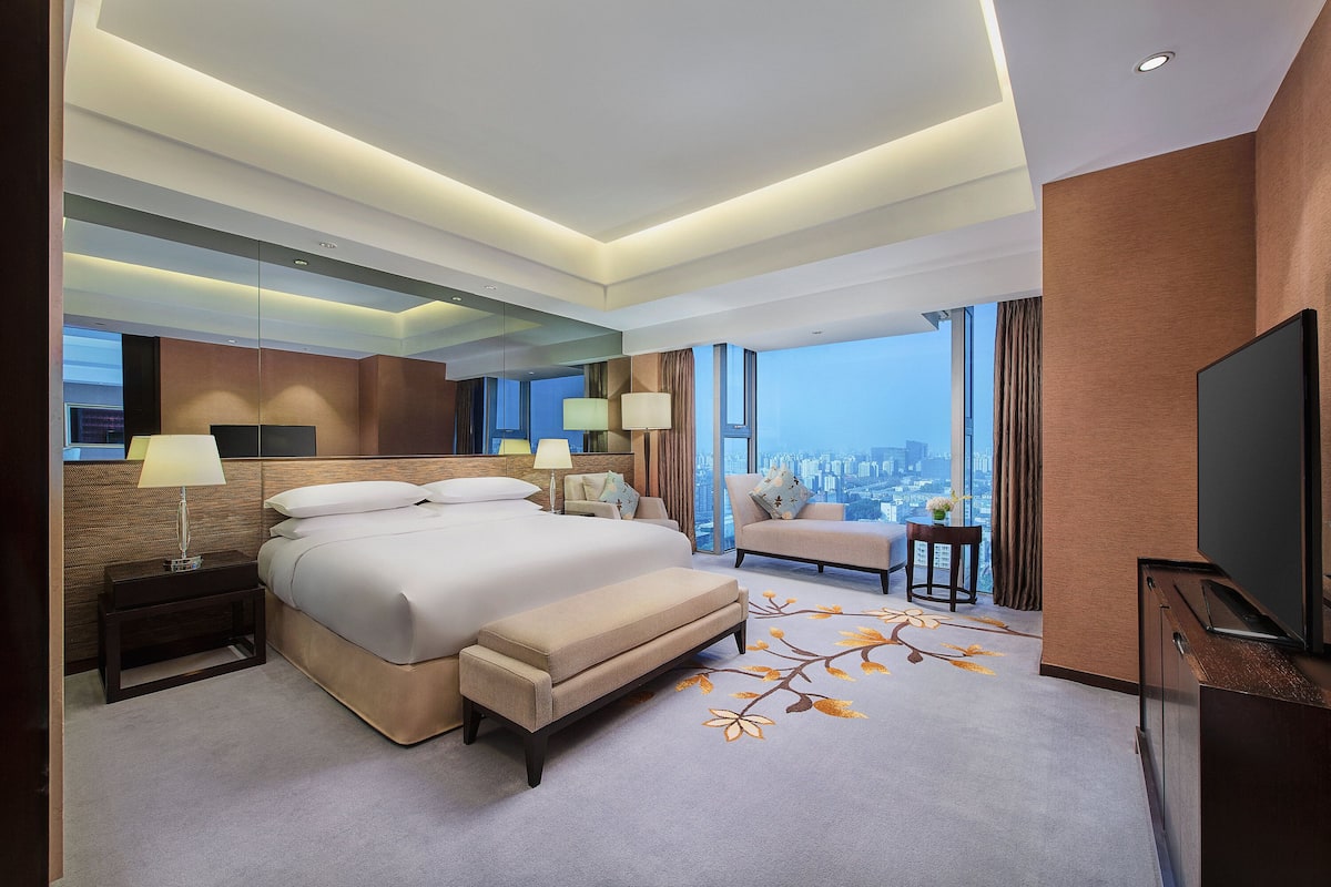 Una habitación de hotel moderna con una cama grande, un sofá, un televisor y vistas a la ciudad.