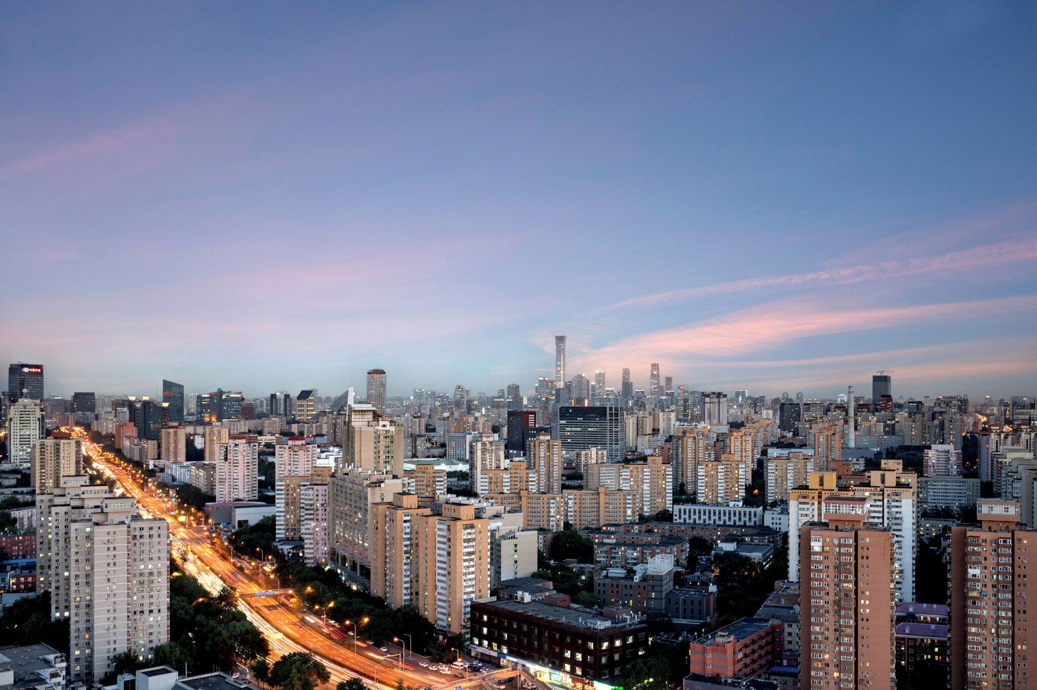 A cityscape with high-rise buildings, a busy road, and a clear sky.