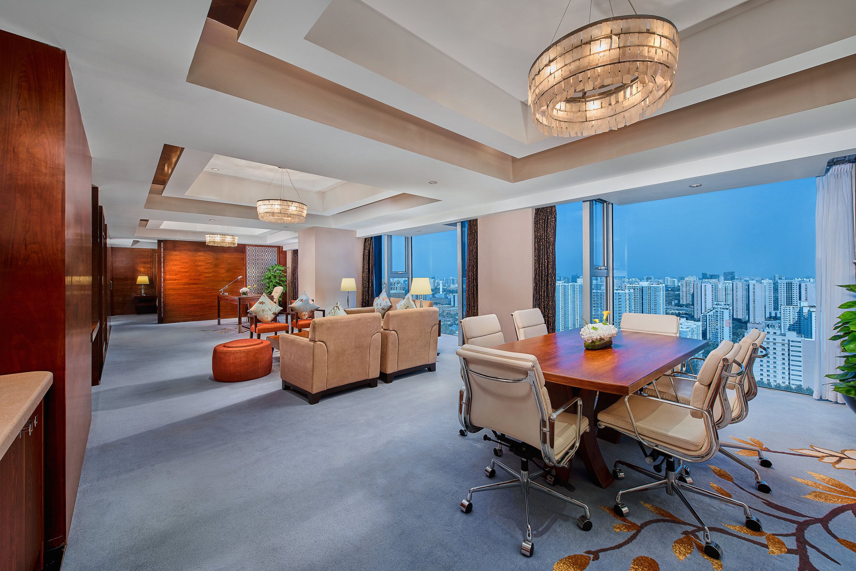 A modern hotel room with a city view, a conference table, and a seating area.