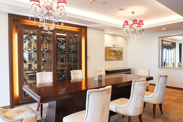 A dining area with a large wooden table, white upholstered chairs, and a wine cabinet filled with bottles.