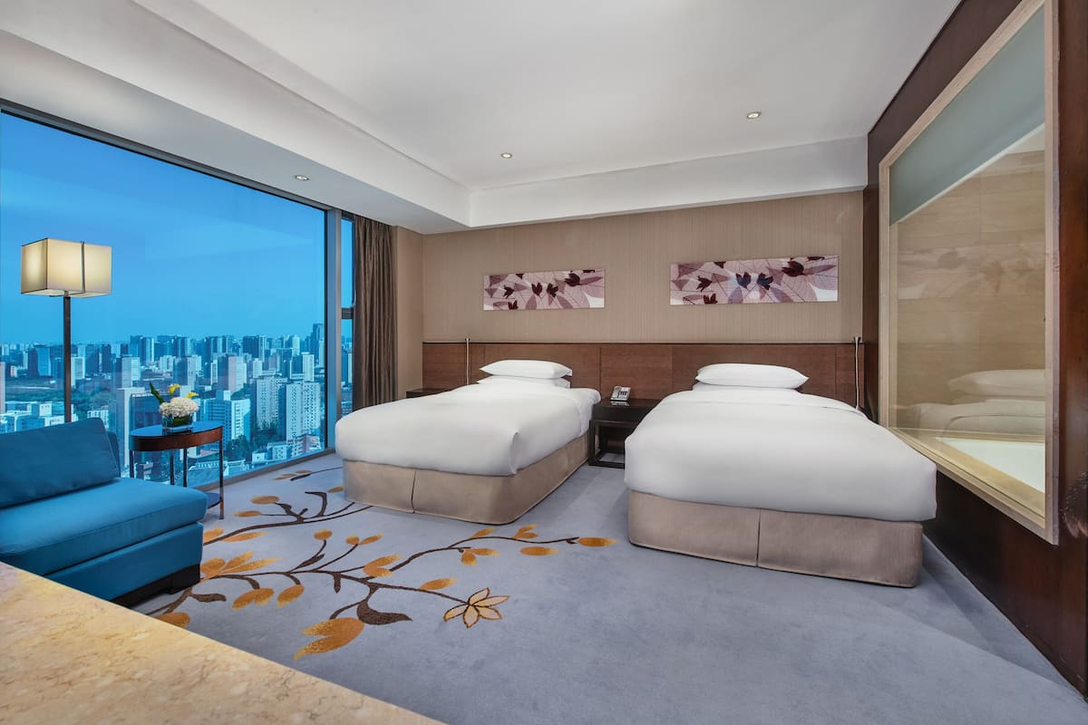 Habitación de hotel con dos camas, un sofá, vista a la ciudad y obras de arte en las paredes.