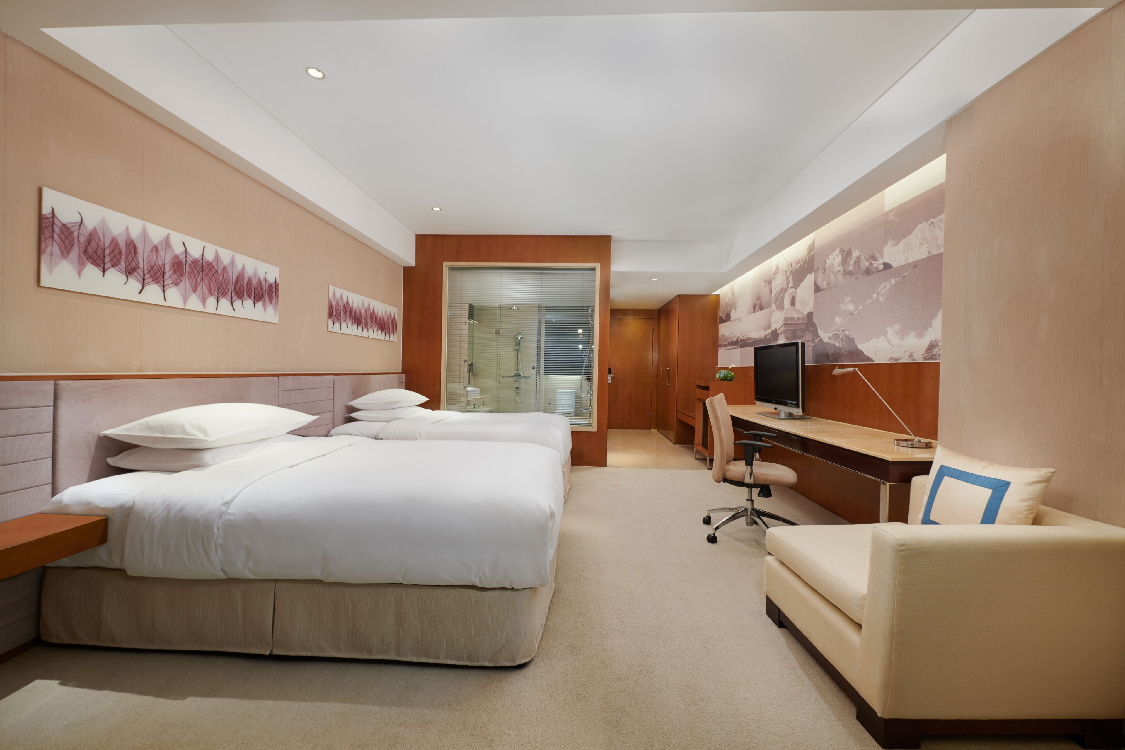 A modern hotel room with a large bed, a desk, a chair, and artwork on the walls.