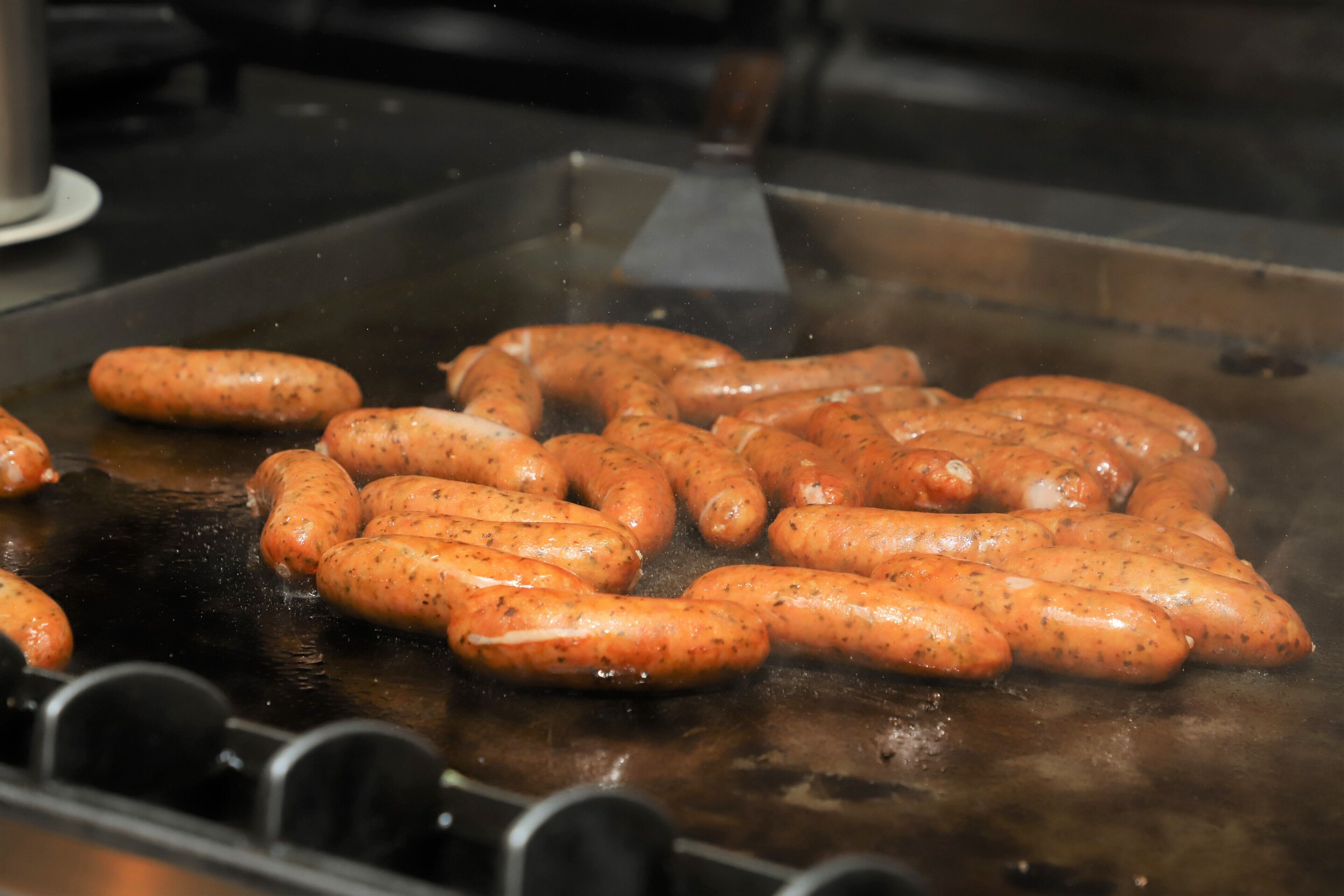 Sausages being grilled on a flat cooking surface.