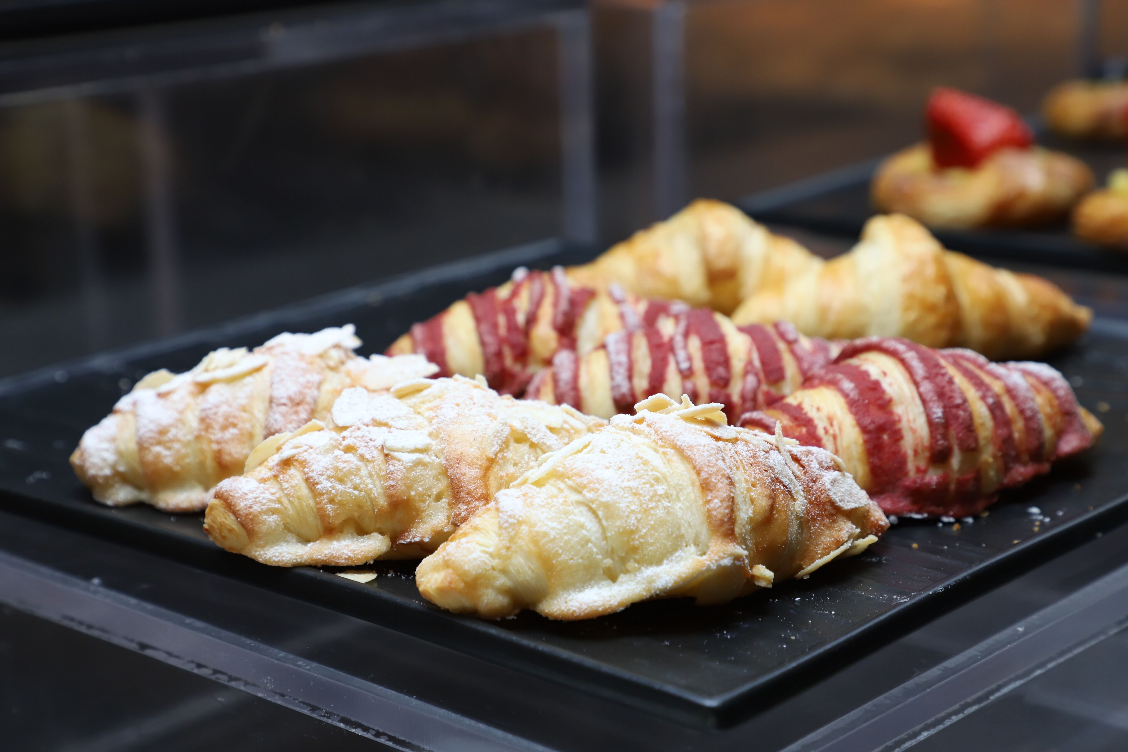 A display case with pastries, including croissants and a red and white striped pastry.