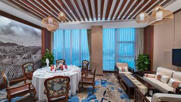 Habitación de hotel con comedor, un conjunto de sofás y un ventanal con vistas a la ciudad.