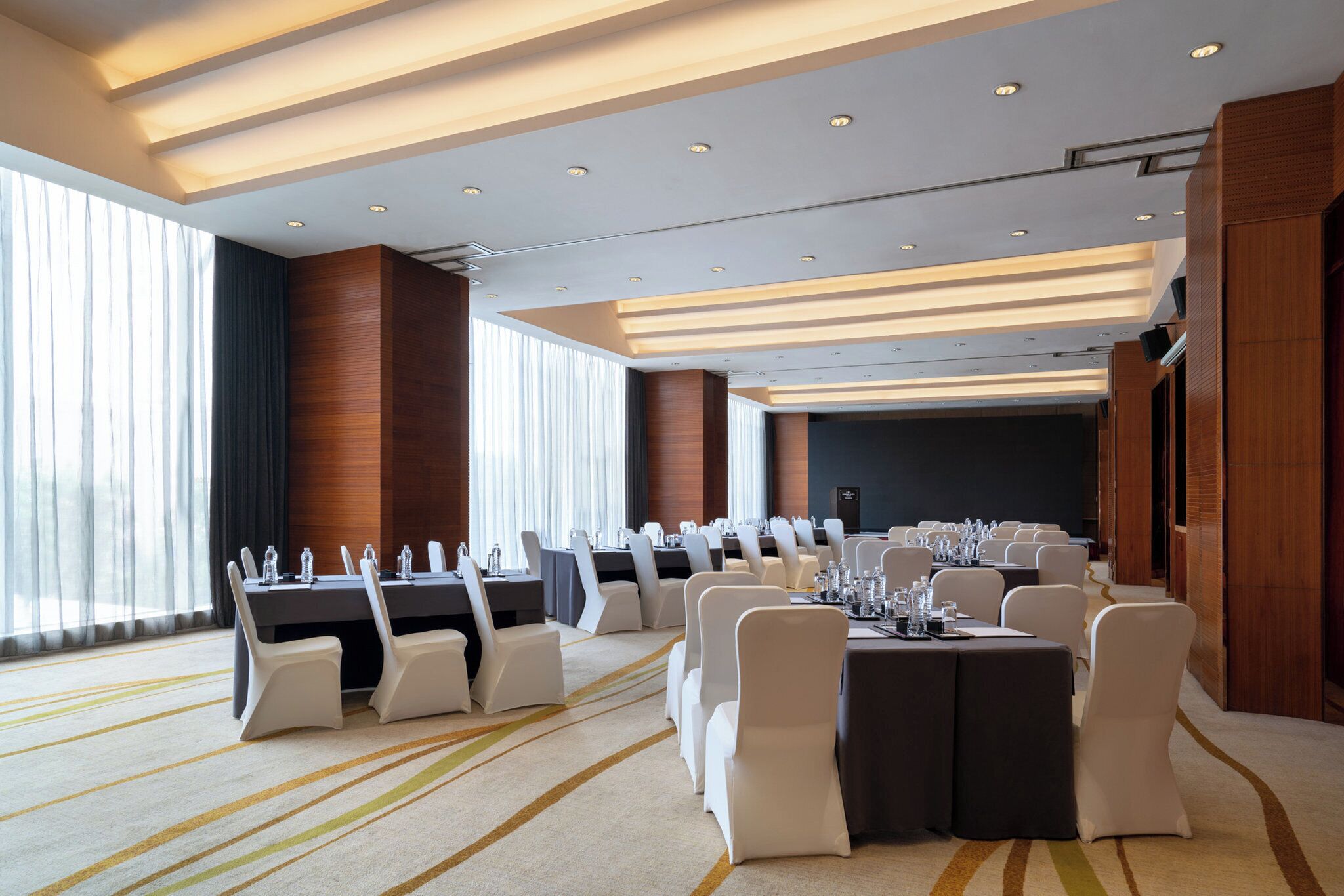 Un salón de conferencias con filas de mesas y sillas, ventanas amplias y un diseño moderno del techo.
