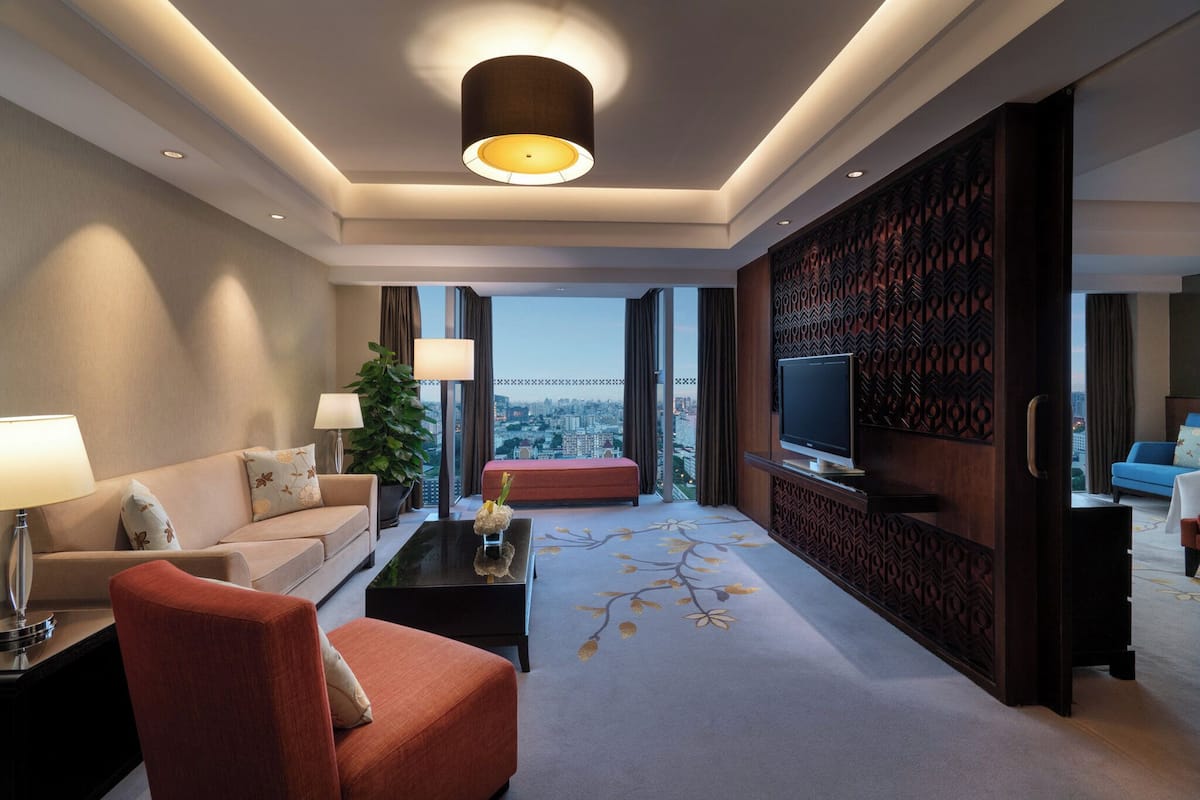 Una habitación de hotel moderna con sofá, sillón, mesa de centro y televisión.