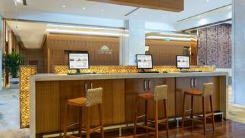 Un área de recepción con un mostrador de madera, tres taburetes de bar y dos pantallas digitales mostrando información.