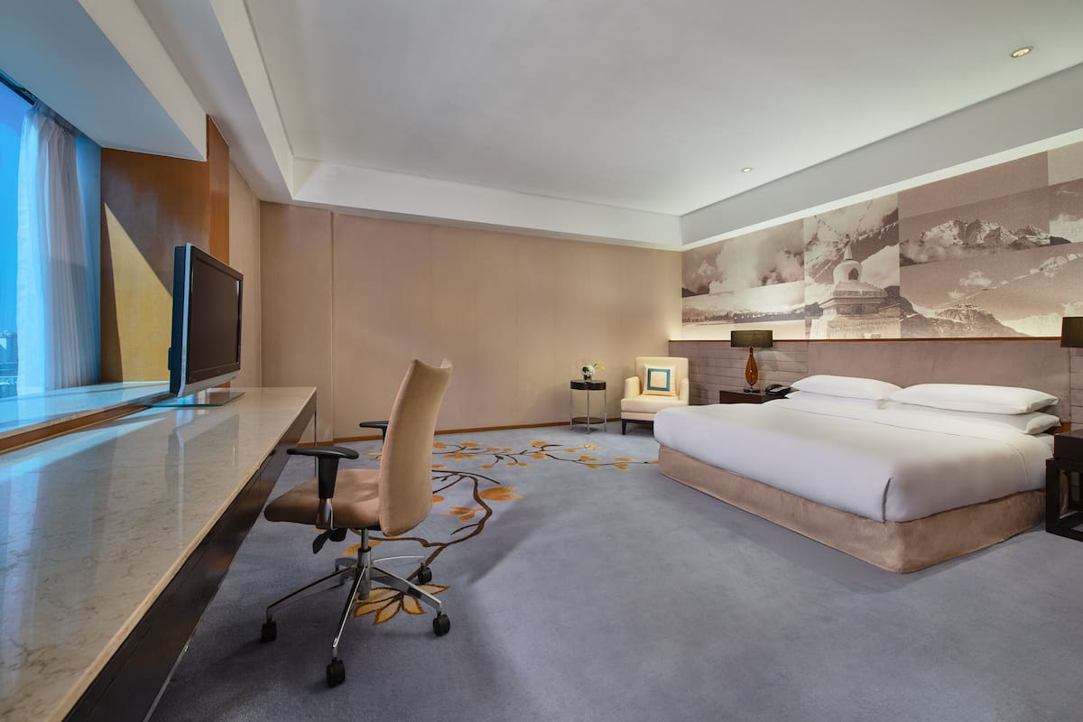 Una habitación de hotel moderna con una cama grande, un escritorio con una computadora, una silla y un ventanal amplio.