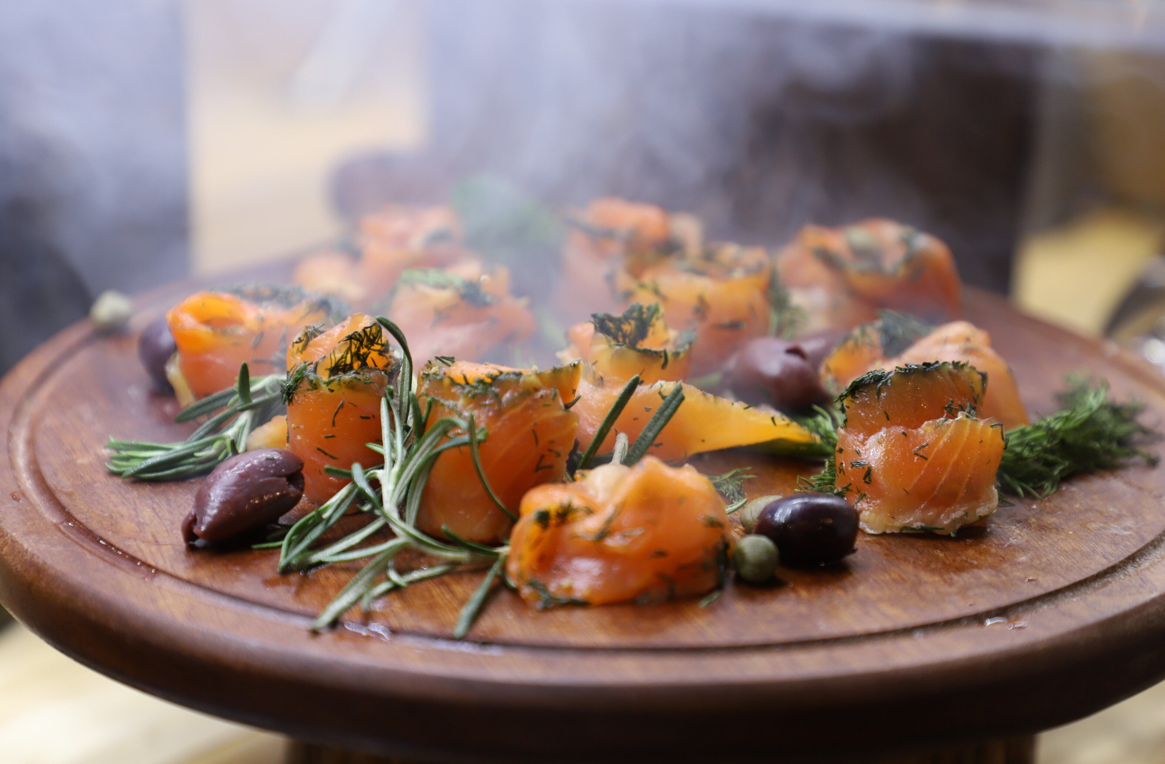 A wooden platter with smoked salmon, olives, and herbs.