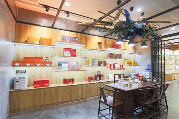 Zona de recepción con mostrador de madera, estantes con diversos objetos y una mesa con sillas.
