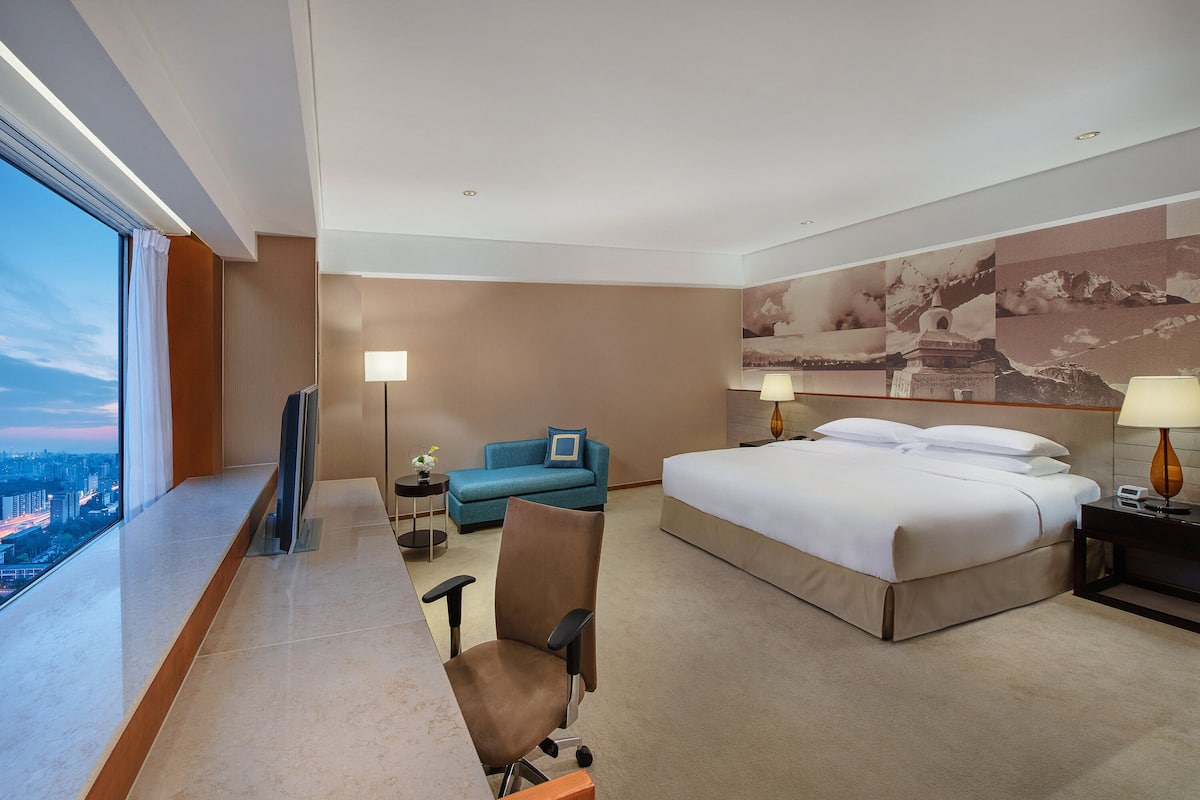 Una habitación de hotel con una cama grande, un escritorio con una silla, un sofá y vista a la ciudad.