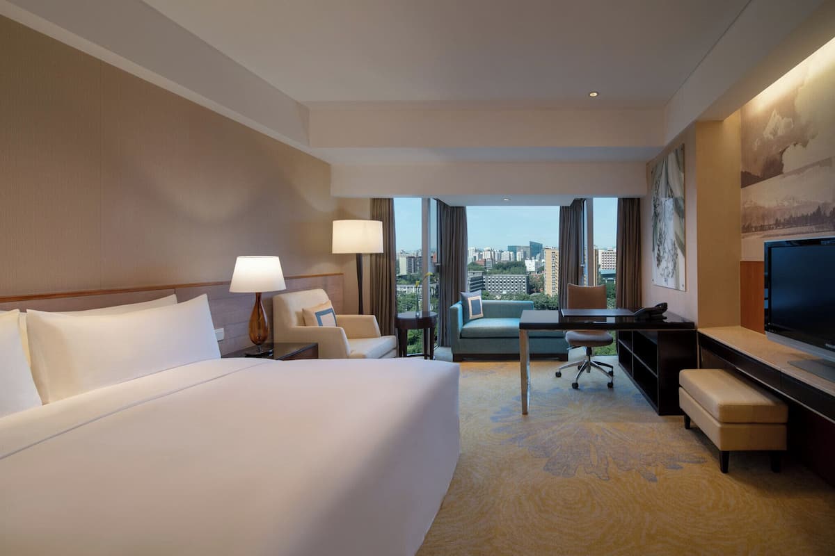 Habitación de hotel con una cama grande, un escritorio, una silla, un televisor y vistas a la ciudad.