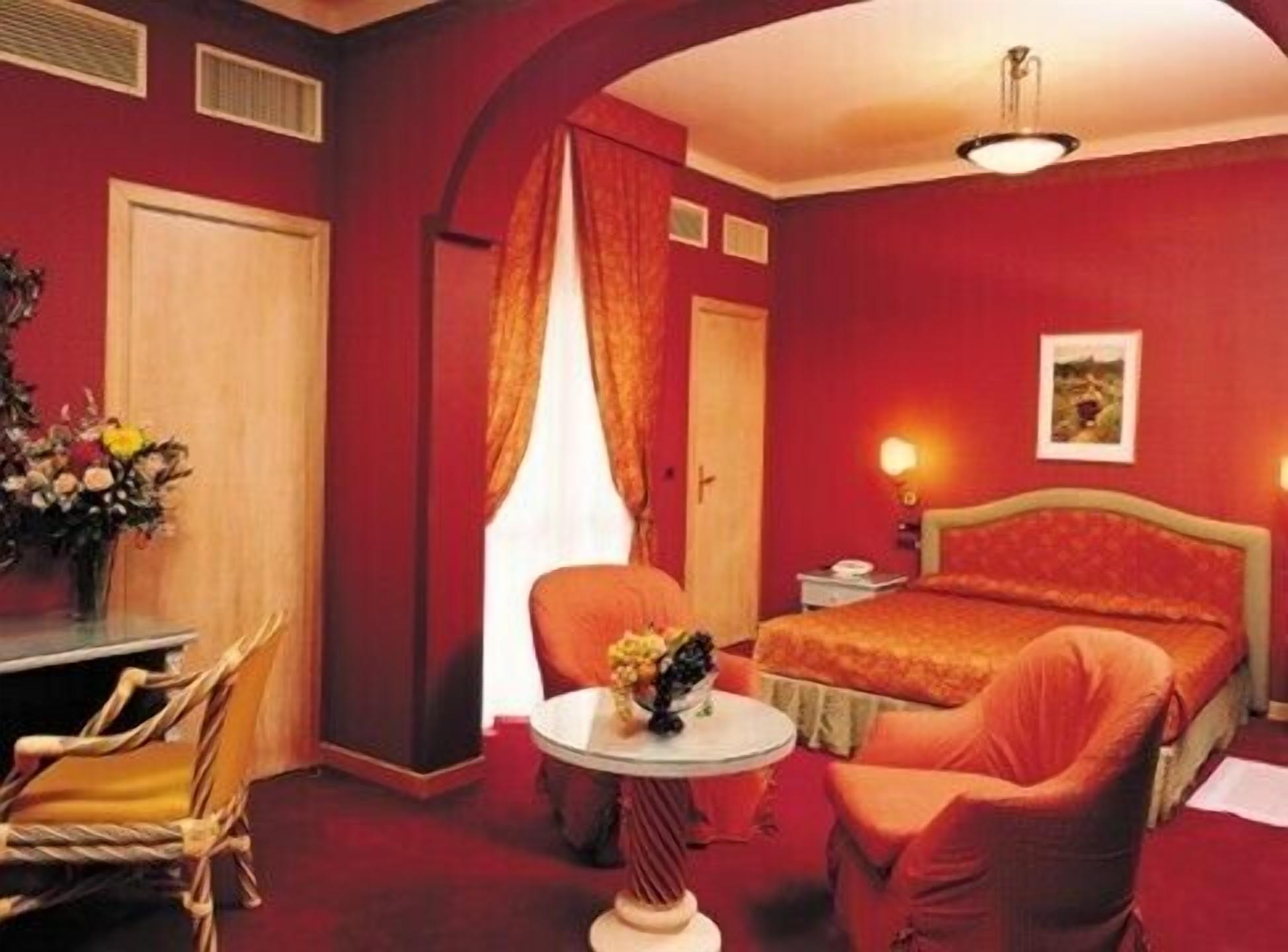 A hotel room with a bed, a desk, a chair, and a small table with flowers.