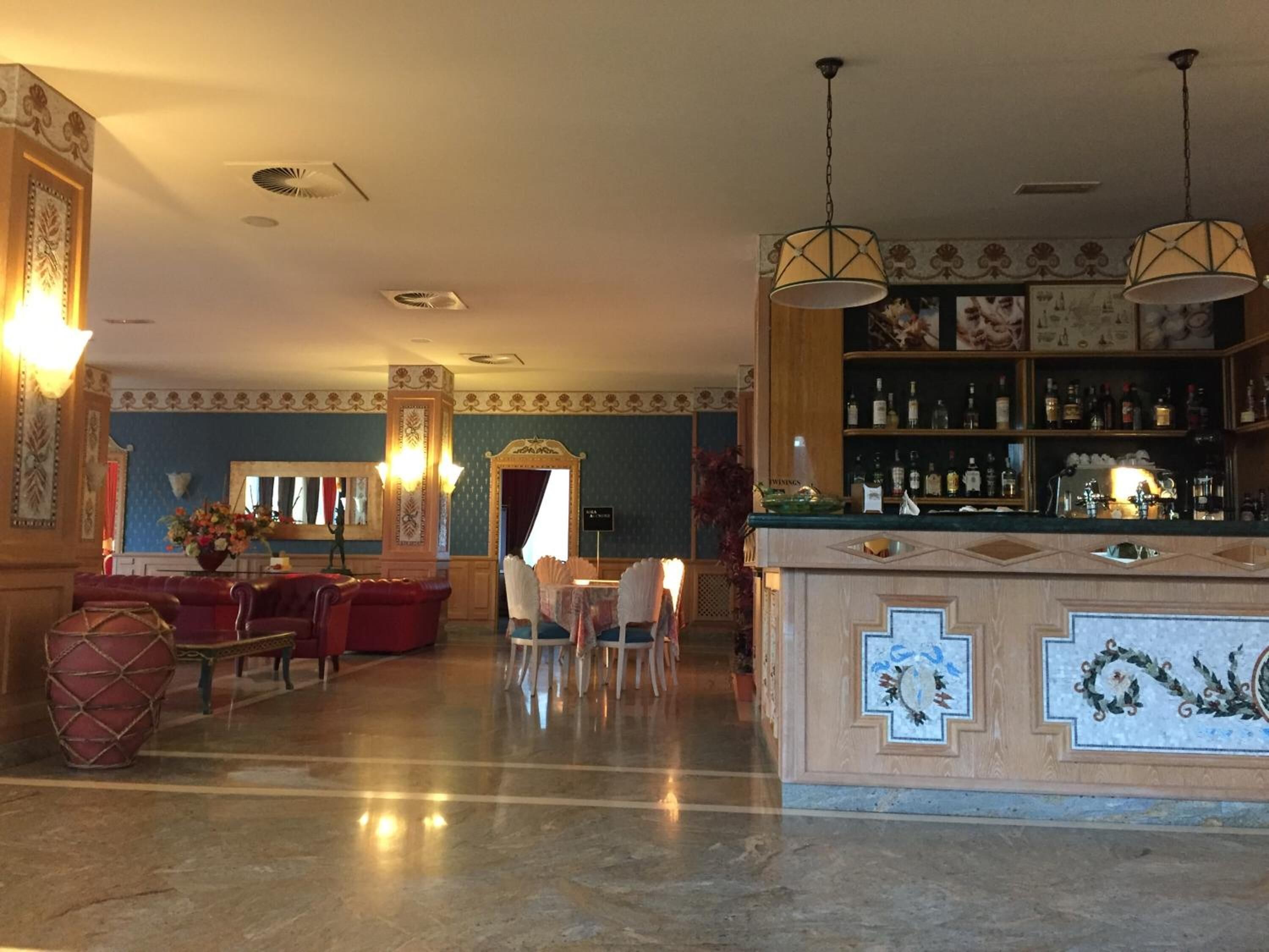 Eine Bar mit Marmorboden, einer Bar, deren Tresen ein dekoratives Fliesenmuster aufweist, und einer Sitzecke mit einem roten Sofa und Sesseln.