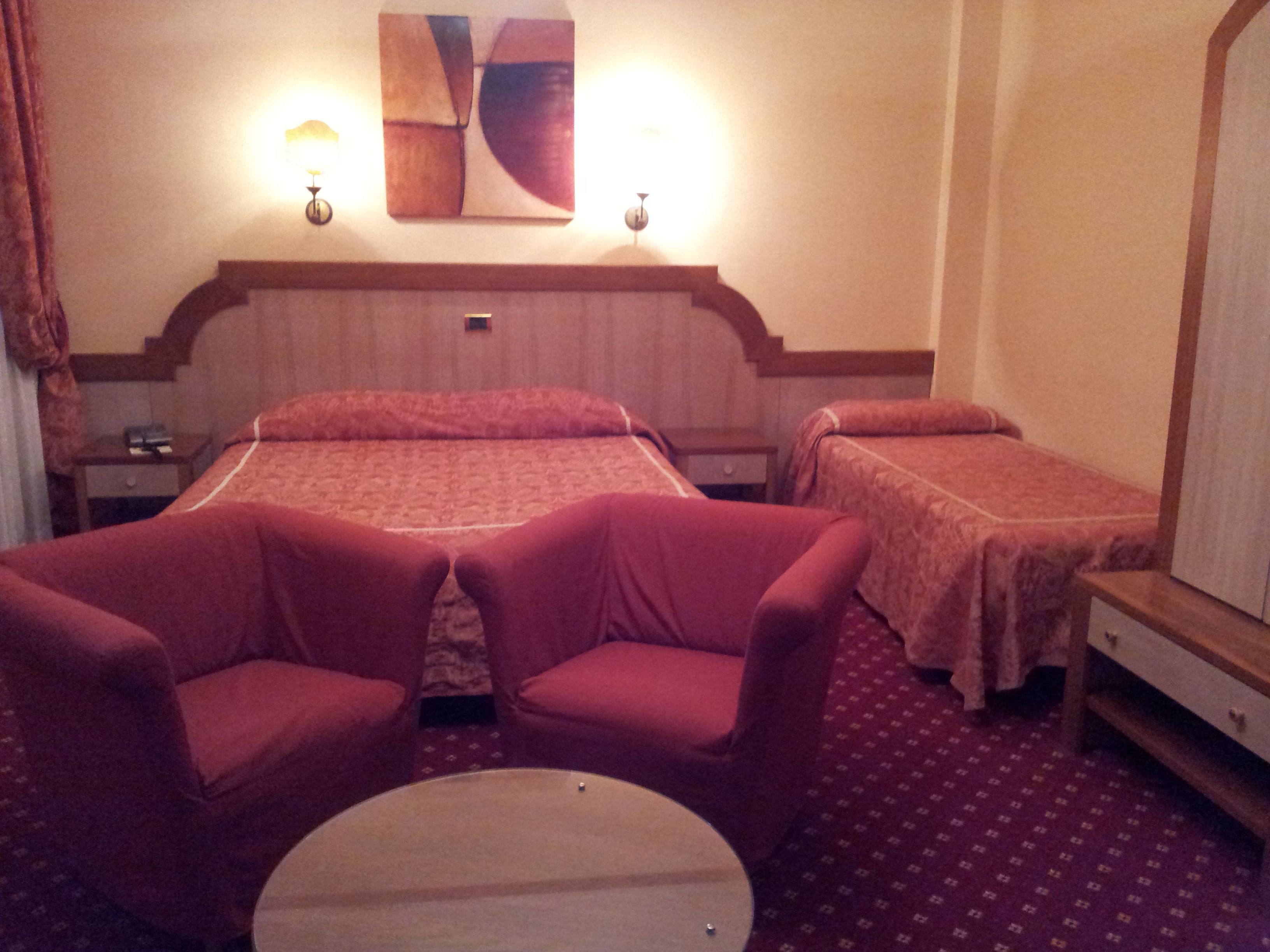 Quarto de hotel com uma cama grande, duas camas de solteiro, uma mesa redonda e duas poltronas.