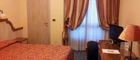 A hotel room with a bed, a desk, a chair, a lamp, and a television.