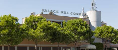Hotel llamado "Palace del Conero" con un letrero llamativo, una zona de estacionamiento y árboles circundantes.