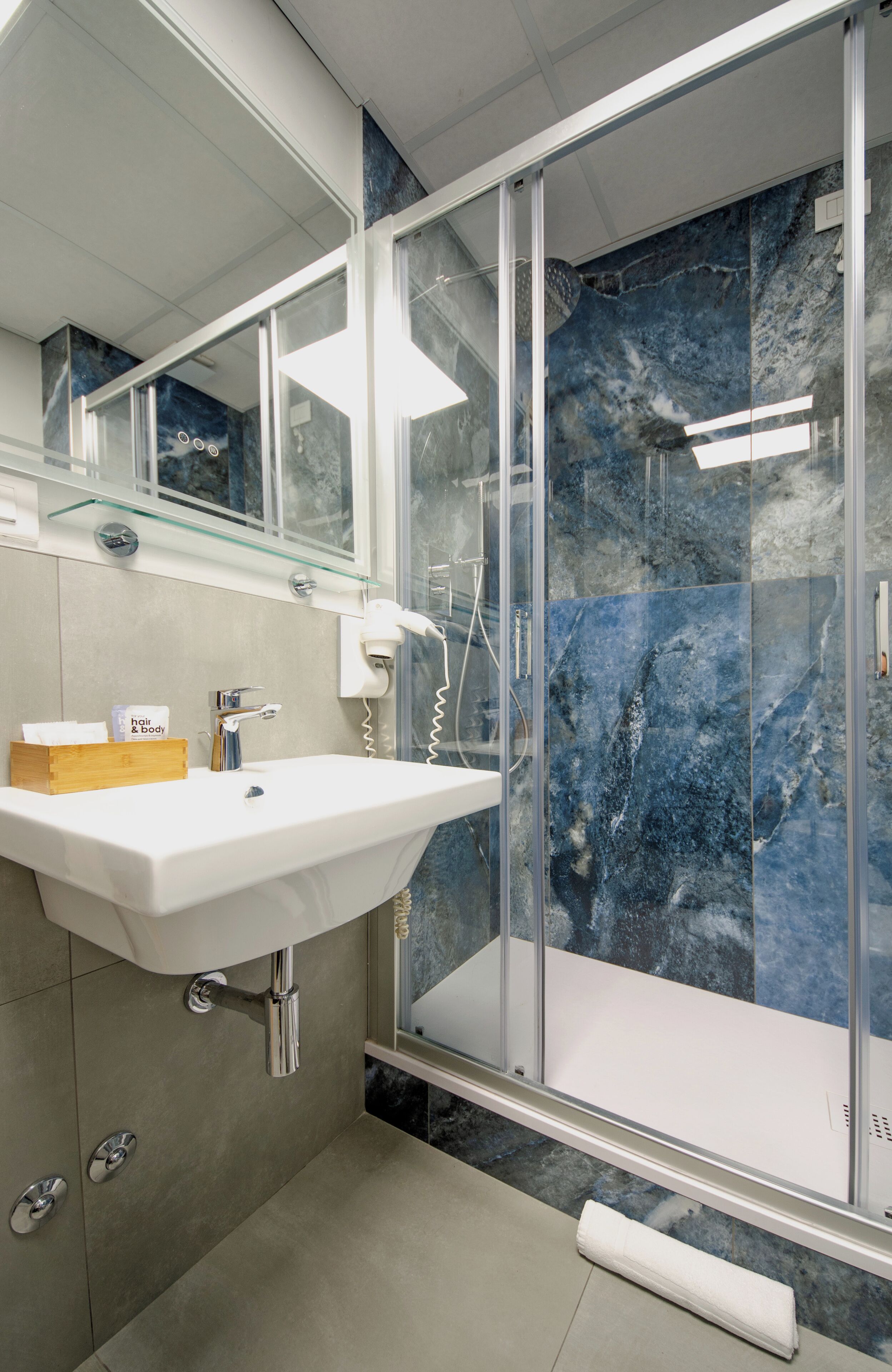Un baño moderno con lavamanos blanco, cabina de ducha de vidrio y paredes de mármol.