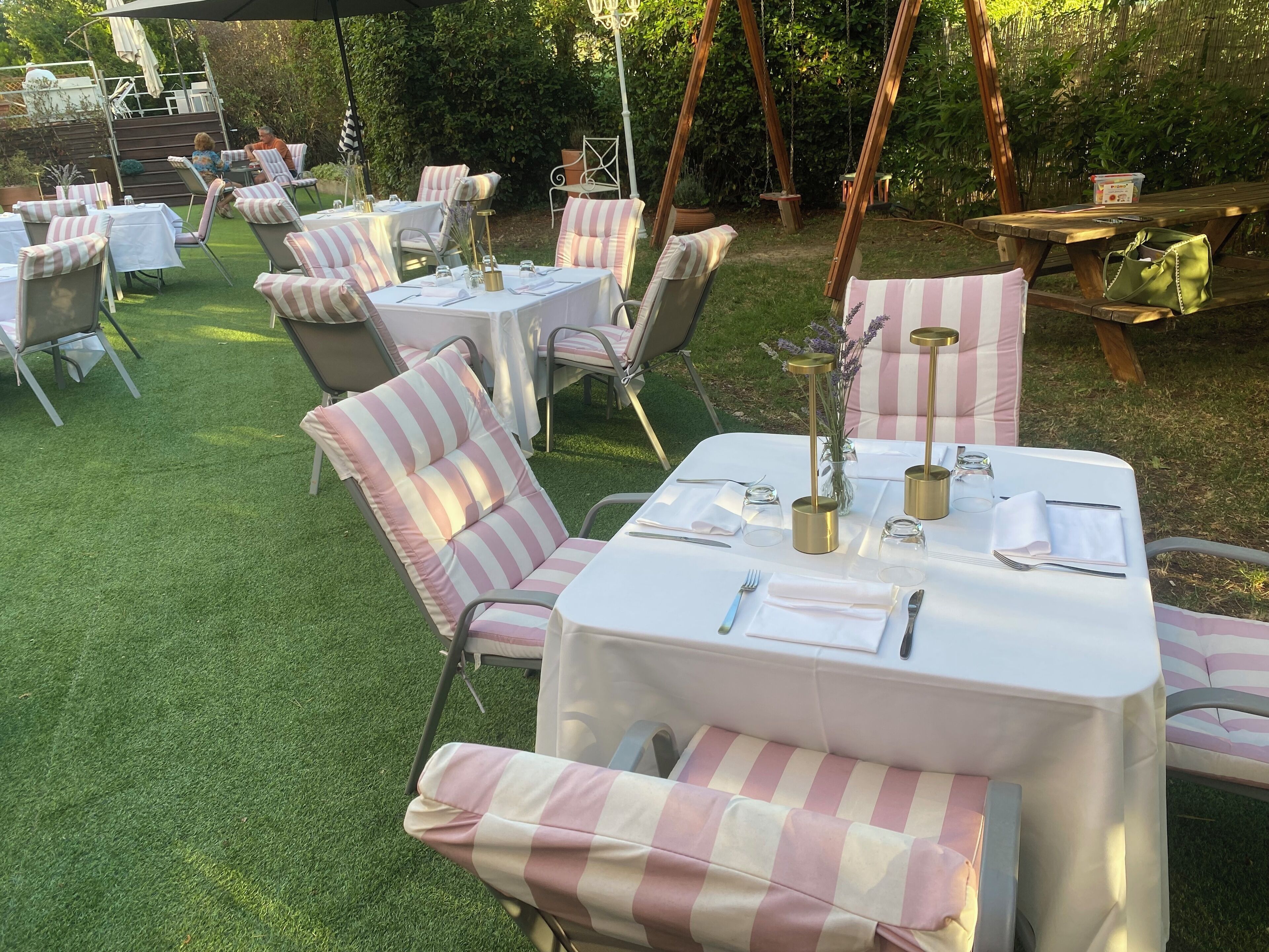 Un área de comedor al aire libre con mesas y sillas, algunas con cojines a rayas.