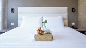 Ein ordentlich bezogenes Bett mit weißen Leinentüchern, ein Holzblock mit einer Tasse und Gebäck, und eine Vase mit einer Blume.