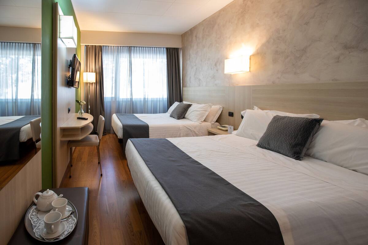 A hotel room with two beds, a sitting area with a table, a small bathroom, and a view of the city.