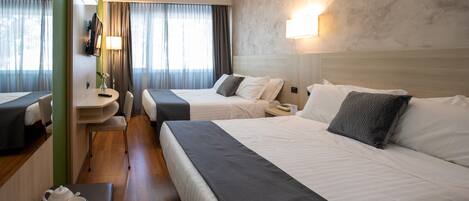 A hotel room with two beds, a sitting area with a table, a small bathroom, and a view of the city.