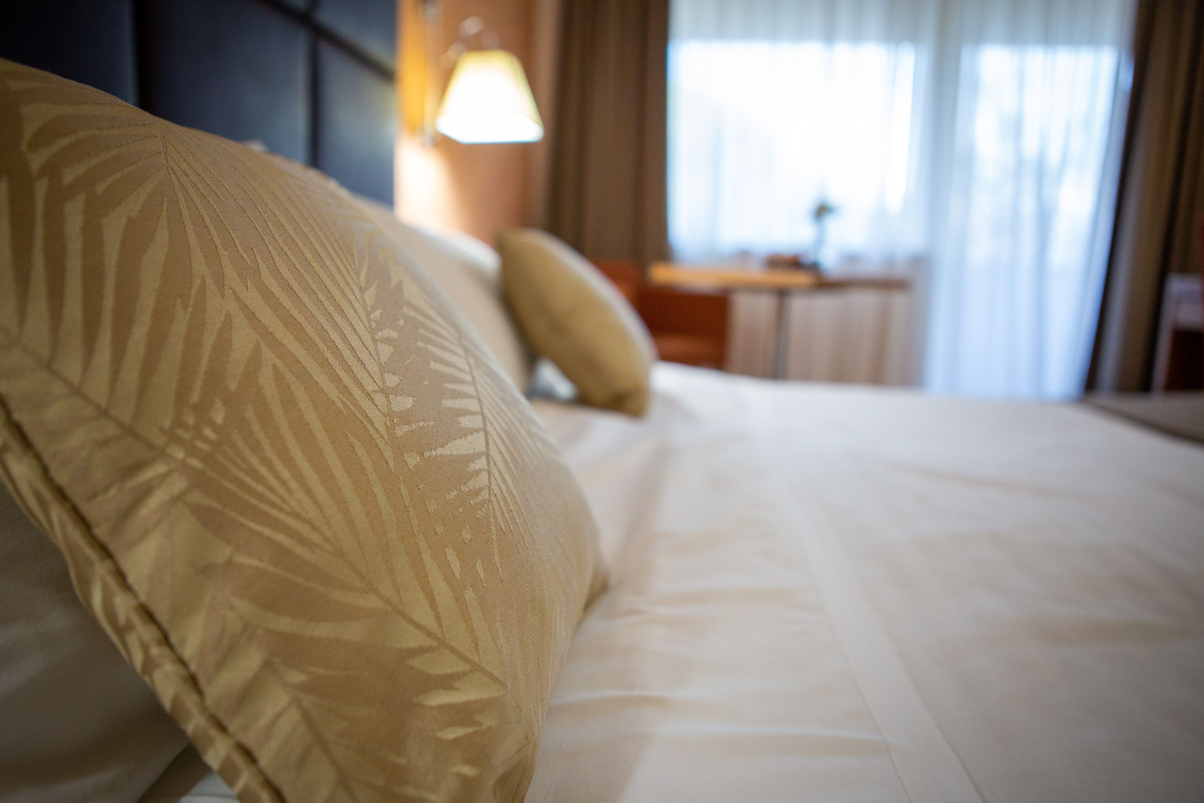 Una habitación de hotel con una cama bien hecha, una mesita de noche y una lámpara.
