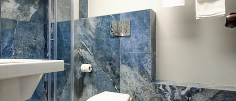 Un baño con pared de mármol, inodoro, bidé y cabina de ducha de vidrio.