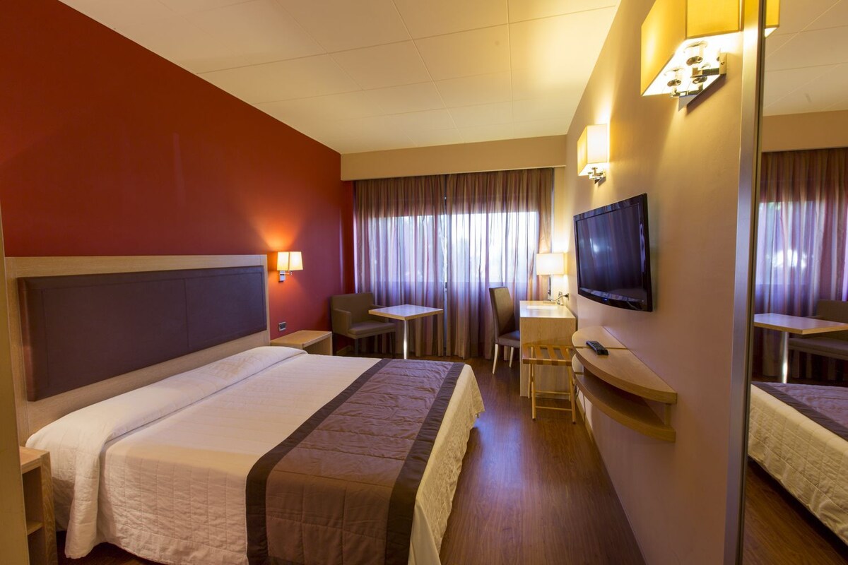 A hotel room with a bed, a desk, a chair, a television, and a mirror.