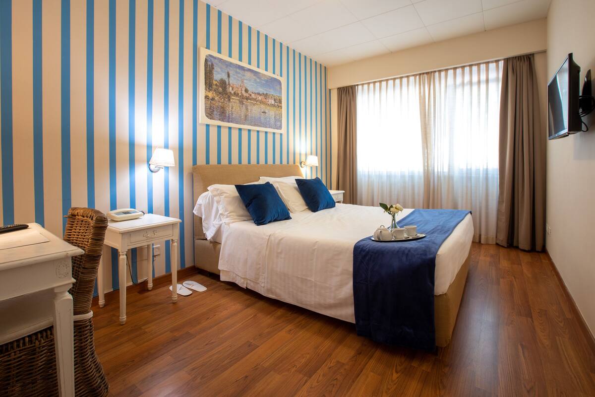 A hotel room with a large bed, a bedside table with a lamp, a chair, and a television on the wall.