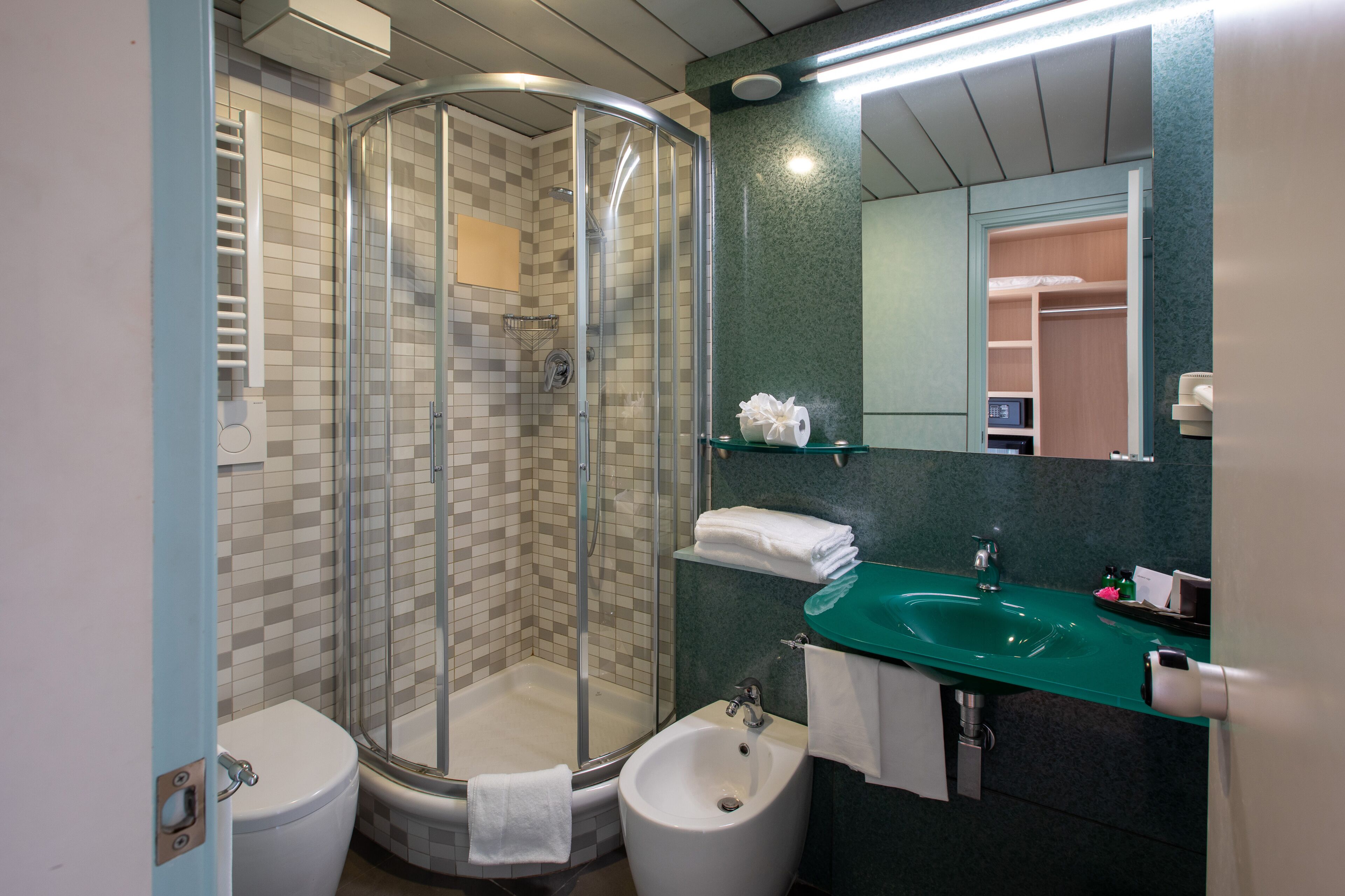 A bathroom with a glass-enclosed shower, a white toilet, a bidet, a green sink, and a mirror above the sink.