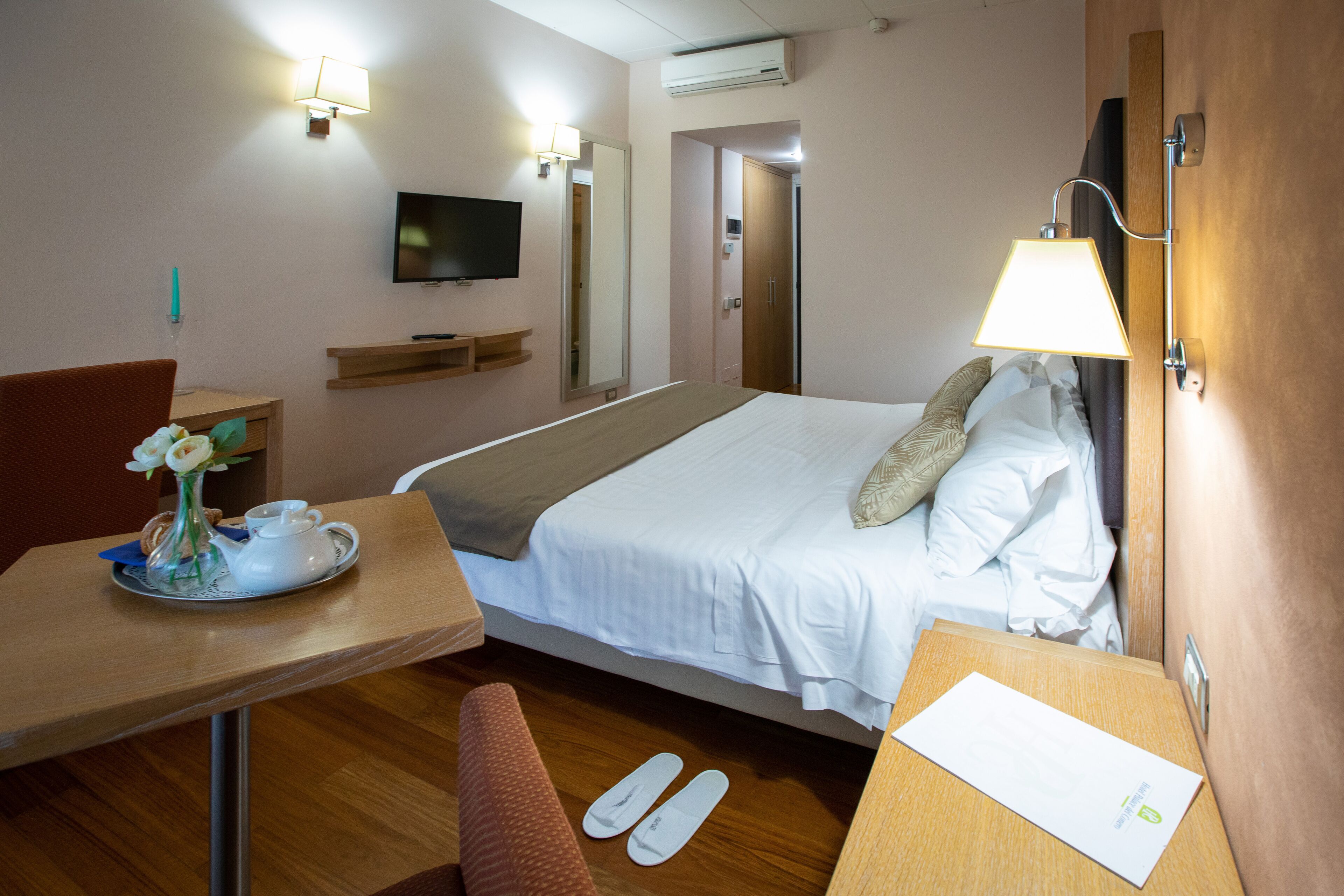 Une chambre d’hôtel avec un lit, un bureau avec une chaise, un téléviseur fixé au mur et une lampe également fixée au mur.