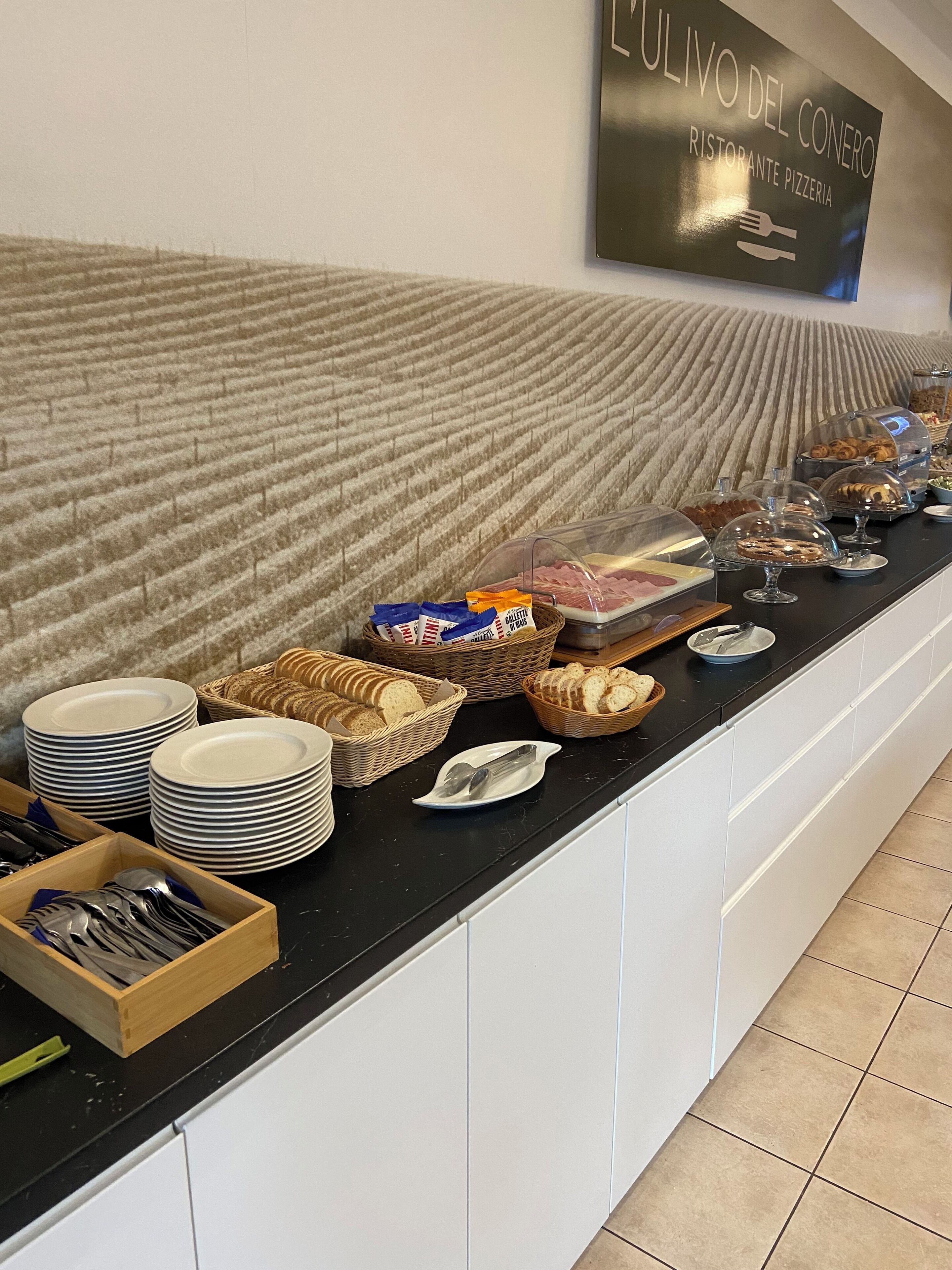 A buffet setup with plates, baskets of bread, and various food items on a counter.