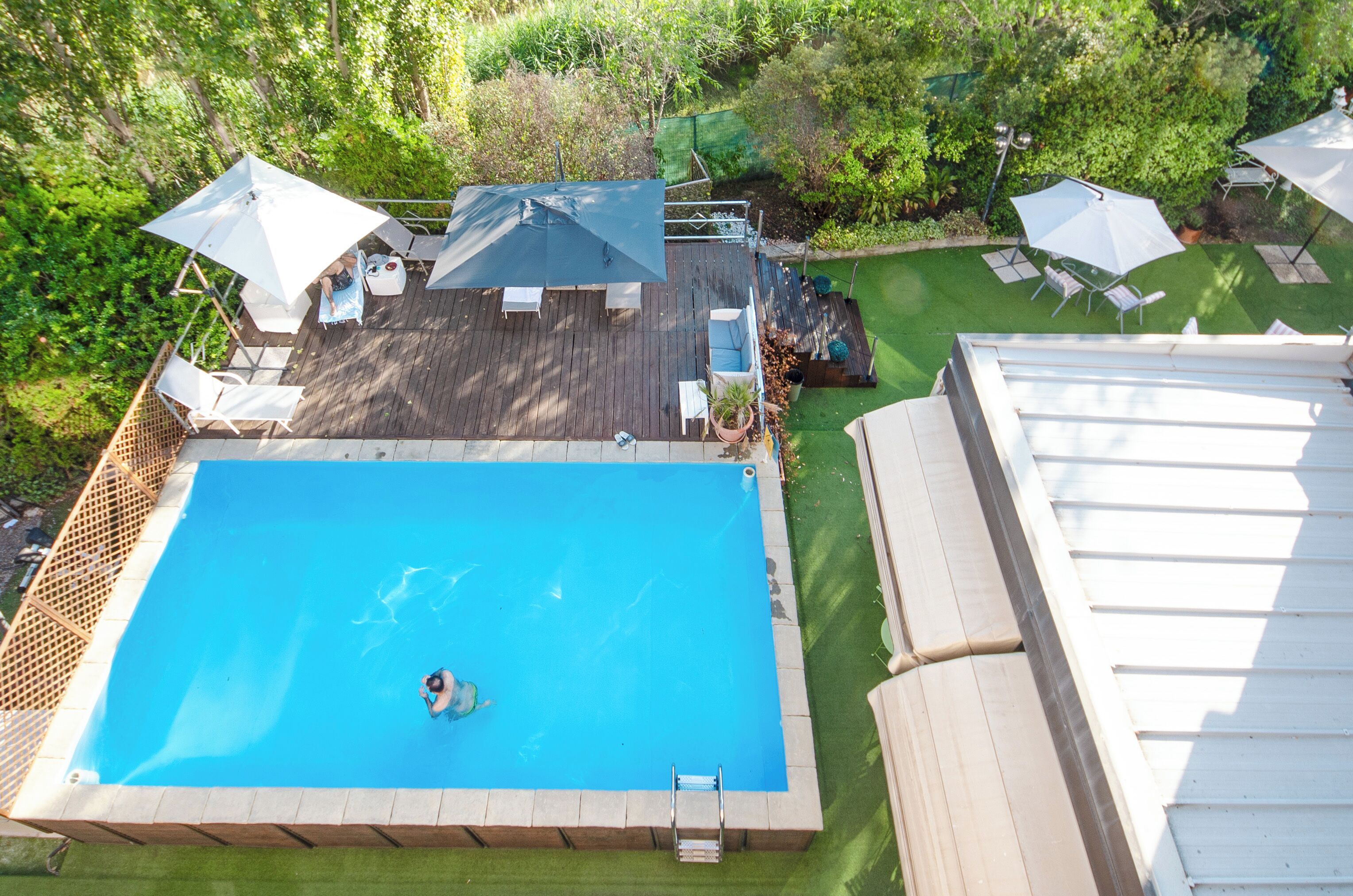 An aerial view of a backyard with a swimming pool, deck chairs, umbrellas, and a small garden area.