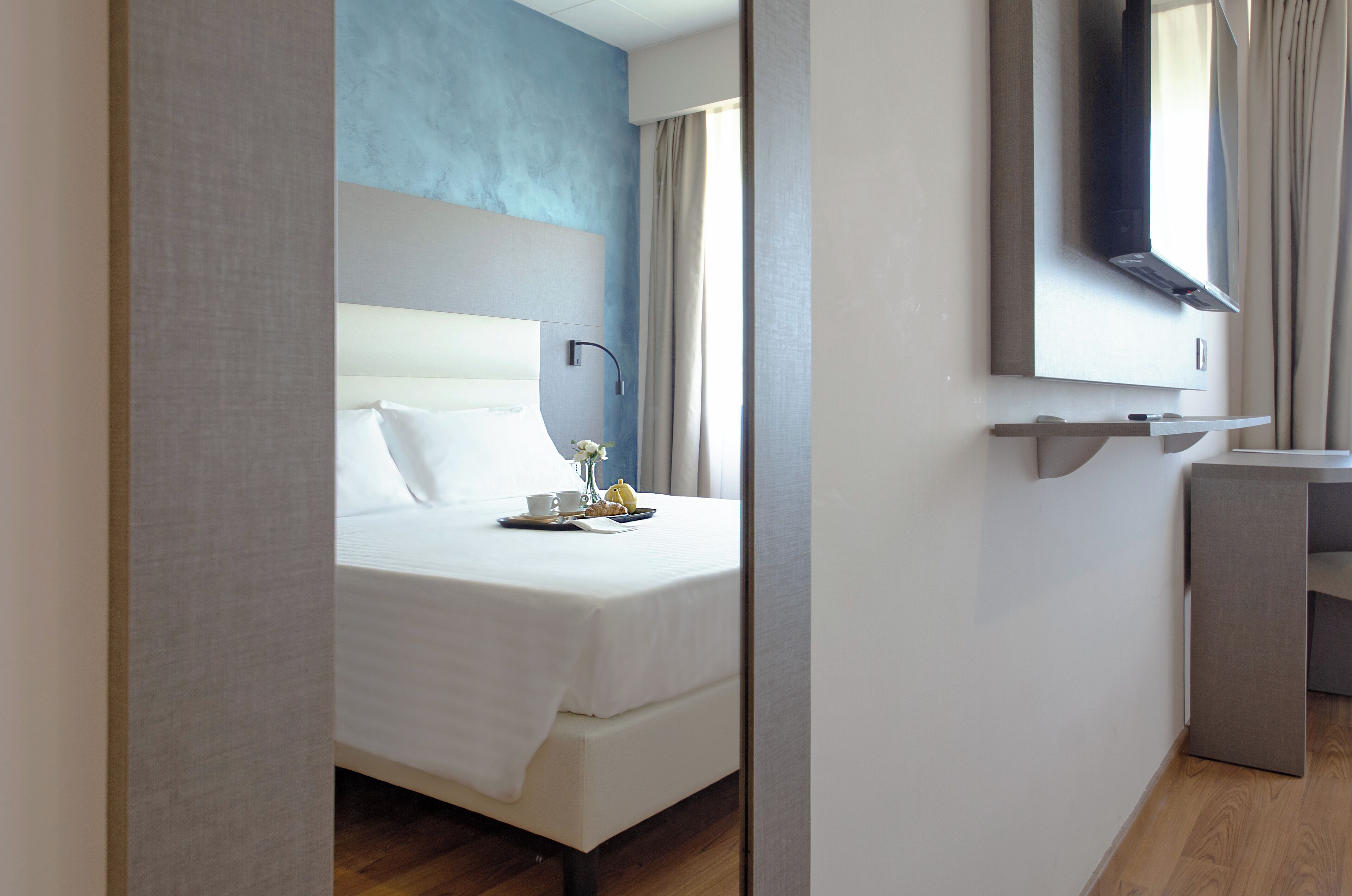 Una habitación de hotel moderna con cama, mesita de noche y un espejo sobre el lavabo.