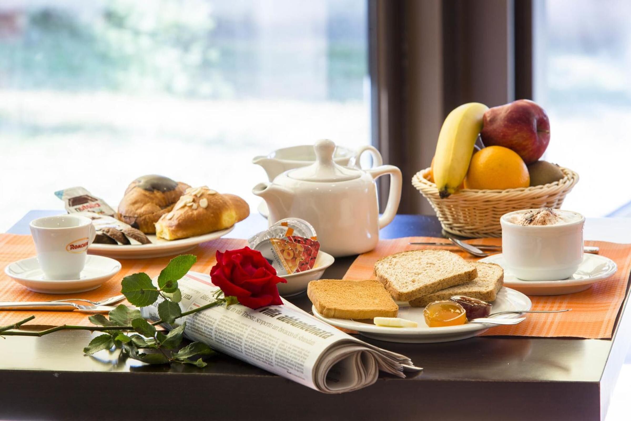 Een ontbijttafel met croissants, een theepot, een fruitmand en een krant.
