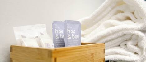 A wooden box containing two toiletry bags labeled "for your hair & body" and a stack of white towels.